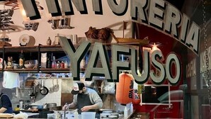 Ravintolan sisustus, jossa on tiskialue, puiset tuolit ja keittiö, joka on näkyvissä ikkunan läpi.