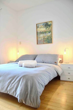A neatly made bed with a grey duvet and pillows, a white bedside table with a lamp, and a painting on the wall. - Warm, quiet & inviting retreat: Steps from Palermo (Buenos Aires)