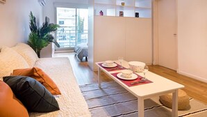 Ein modernes Wohnzimmer mit einer Couch, einem Esstisch für zwei Personen und einer weißen Regaleinrichtung an der Wand.