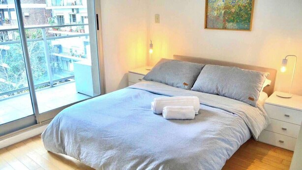 Ein Schlafzimmer mit einem großen Bett, zwei Nachttischen, einem Fenster mit Blick auf Gebäude und einem Bild an der Wand.