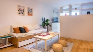 Ein modernes Wohnzimmer mit einer Couch, einem Couchtisch und einer Pflanze. Im Hintergrund steht ein weißes Schränkchen und ein Fernseher.