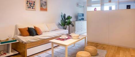 A modern living room with a sofa, a coffee table, and a plant. There is a white cabinet and a TV in the background.