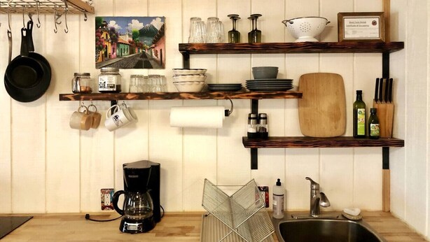 Eine Küche mit Holzböden, die Geschirr, eine Kaffeemaschine und ein Gemälde beherbergt.