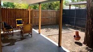 Ein überdachter Patio-Bereich mit Holzmöbeln, einem Betonboden und einem Holzzaun im Hintergrund.