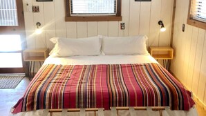 Ein Bett mit gestreifter Bettdecke, zwei Nachttische und ein Fenster mit Jalousien.