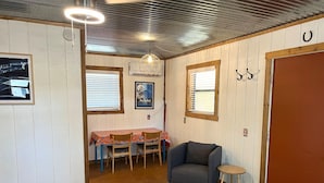 Ein Zimmer mit Esstisch, Stühlen, einem blauen Sessel, einem Hocker und einer Tür.