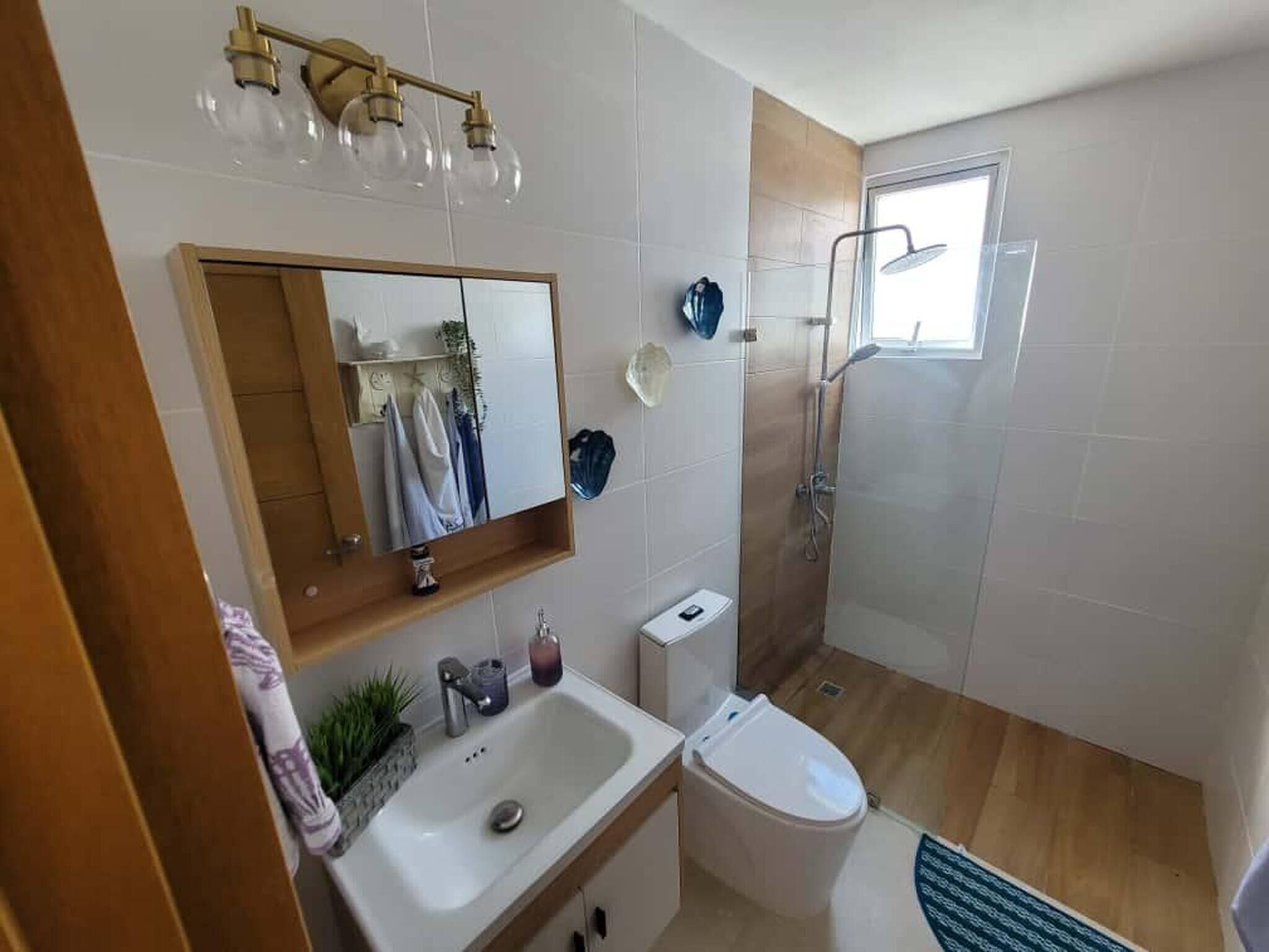 A bathroom with a sink, toilet, and shower. There is a mirror above the sink and a window above the shower.