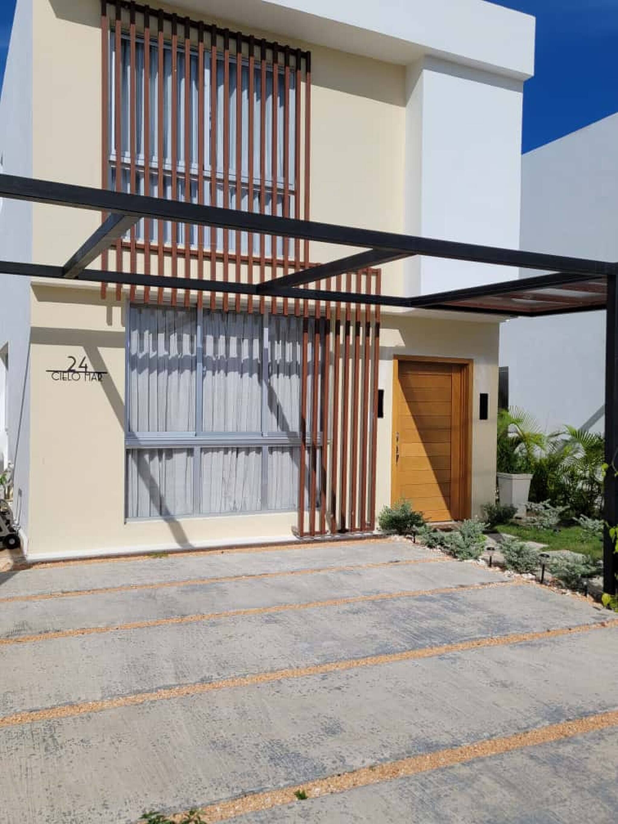 Un edificio moderno de dos pisos con fachada color beige, una puerta de madera y un portón de metal.