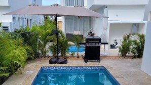 Una piscina amb vora de rajola, envoltada de palmeres i una zona de barbacoa.