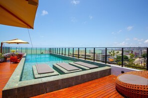 Piscina infinita no terraço com espreguiçadeiras e guarda-sóis, com vista para a cidade.