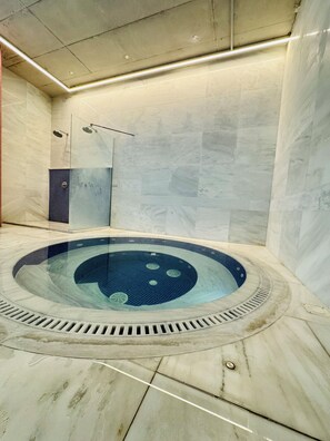 Een wellnessruimte met een jacuzzi, een douche en een betegelde muur.