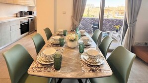 A dining area with a table set for six, green chairs, and a view of the city through large windows. - Luxury 2BR Apt at Elysia Park S6 with Pools, Gym & Spa - Center Paphos (Pafos)