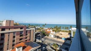 A view from a high-rise building overlooking a coastal area with palm trees, a beach, and the ocean. - Get By Side #702 - Modern Studio by Carpediem (João Pessoa)