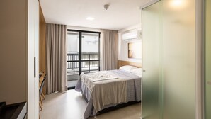 A hotel room with a bed, a desk, and a balcony with curtains. - Get By Side #503 - Studio em Bessa por Carpediem (João Pessoa)
