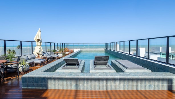 A rooftop infinity pool with lounge chairs and a seating area, offering a view of the ocean. - Get By Side #503 - Studio em Bessa por Carpediem (João Pessoa)