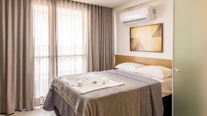 A hotel room with a bed, curtains, an air conditioning unit, and a painting on the wall. - Get By Side #503 - Studio em Bessa por Carpediem (João Pessoa)