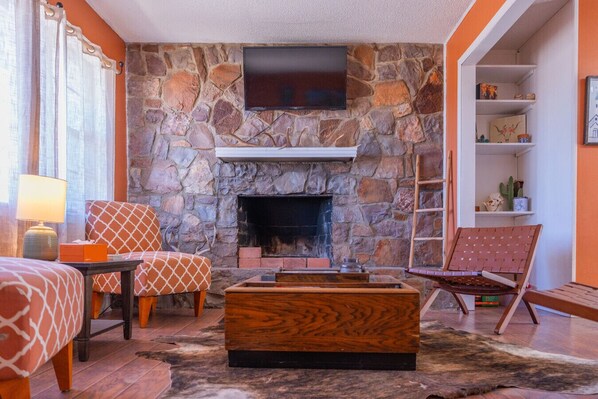 A cozy room with a stone fireplace, a flat-screen TV, and a comfortable seating area with patterned chairs and a wooden coffee table.