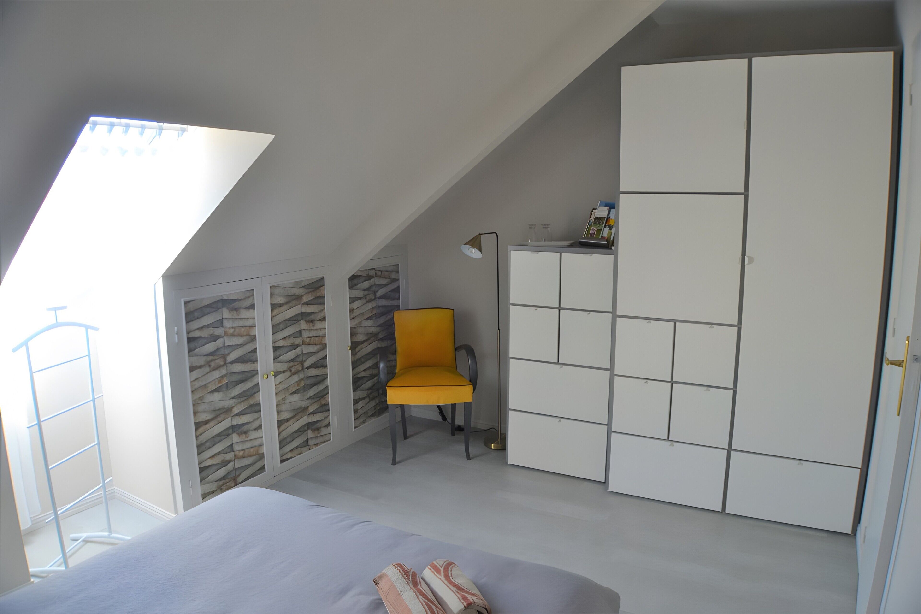 Une chambre avec un plafond en pente, un lit, une armoire, une chaise et une petite table.