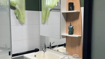 Un baño con lavamanos blanco, espejo y repisa de madera con un jarrón.