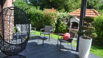 Eine Terrassengruppe im Freien mit einem runden Stuhl aus Draht, einem kleinen Tisch und zwei Sitzgelegenheiten mit Kissen.