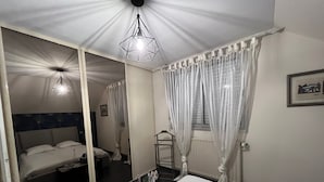 Et soveværelse med seng, sengebord, spejl og en hængende lampe.
