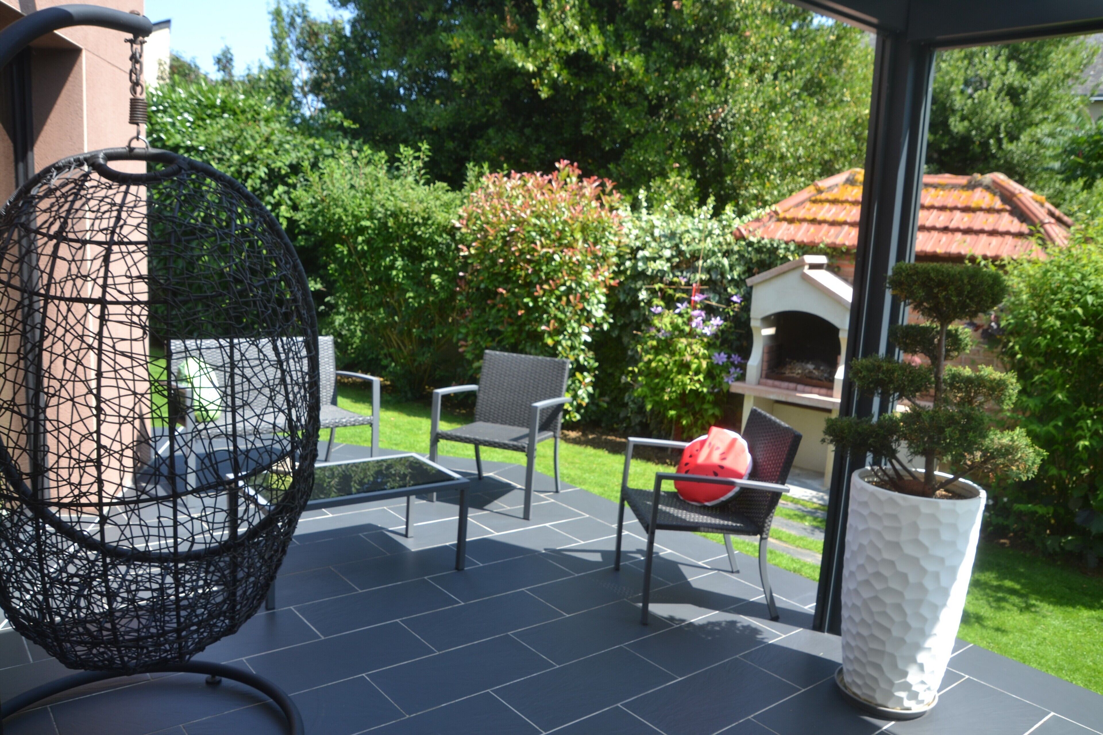 An outdoor patio with a round, wire-framed chair, a small table, and two chairs with cushions.