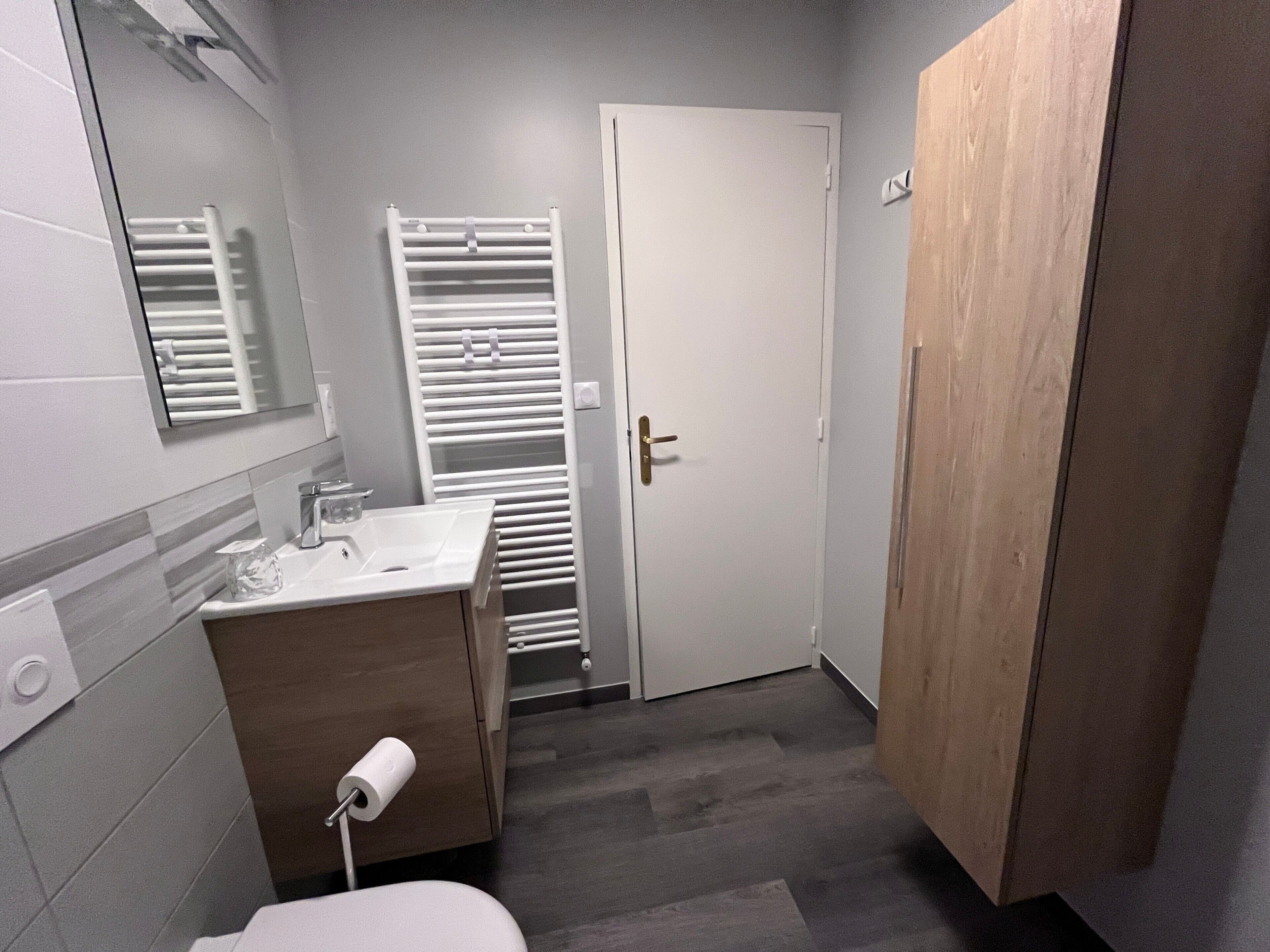 Une salle de bain comprenant des toilettes, un lavabo, un miroir, un porte-serviettes et une porte.