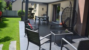 En overdækket terrasse med et bord og stole, en hængestol og et lille bord med en dekorativ genstand.