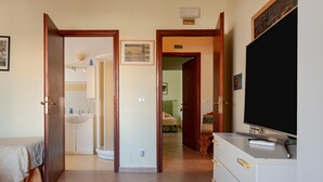 A hotel room with a bed, a TV, a dresser, a bathroom with a sink, and a hallway leading to another room. - 'Bandb Cindy - Yellow Room' with Shared Garden, Wi-Fi and Air Conditioning (Navacchio)