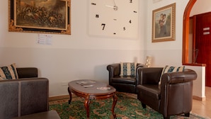 Ein Zimmer mit einer großen Wanduhr, zwei Ledersofas, einem kleinen Holztisch und einem gemusterten Teppich.