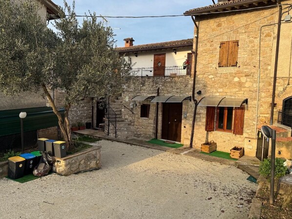 Un patio con edificios de piedra, un árbol y un contenedor de basura.