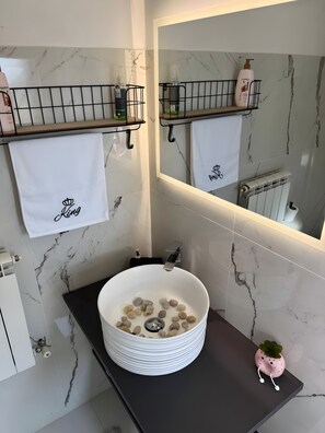 A bathroom with a white marble sink, a mirror, and two towel racks with white towels.