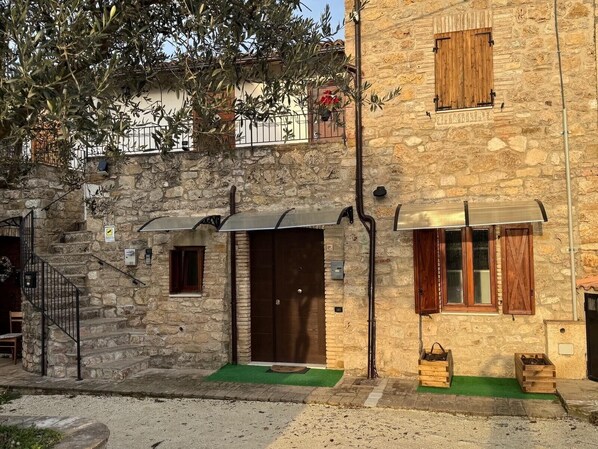 A stone building with a wooden door, a small window, and a staircase leading to an upper level.