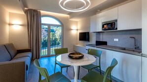 A modern kitchen with a built-in oven, a flat-screen TV, and a dining area with a round table and green chairs. - Villa Pignone 12 (Genova)
