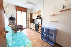 A compact living space with a bed, a kitchenette, a dining area, and a ceiling fan. - CV019 – Cervia, one-bedroom apartment with balcony and parking space (Cervia)