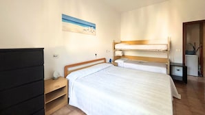Ein Zimmer mit einem Einzelbett, einem Nachttisch, einem Schreibtisch, einem Deckenventilator und einem Bild an der Wand.