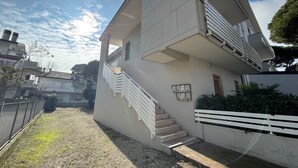 Ein zweistöckiges Gebäude mit einer Treppe zum oberen Stockwerk, einer kleinen Außenanlage mit einer Umzäunung und einem klaren Himmel.