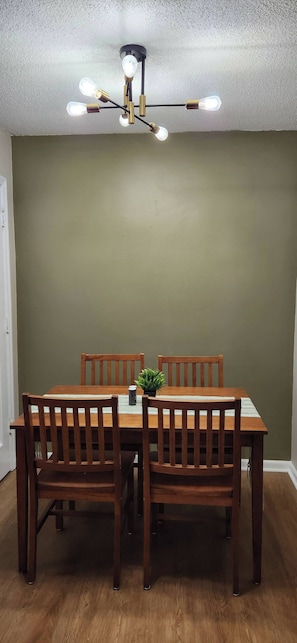 Un comedor con una mesa y sillas de madera, un candelabro en el techo y una pared verde.