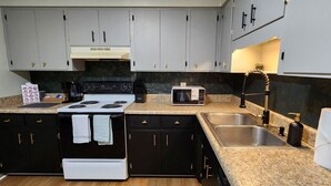 A compact kitchen with a stove, microwave, sink, and granite countertop. - 2BR Near Sherman College & Shops (Boiling Springs)