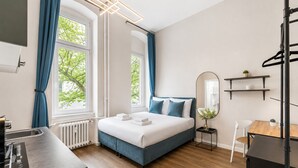 Habitació d'hotel moderna amb un llit, un escriptori, una cadira, un radiador i una finestra amb cortines.