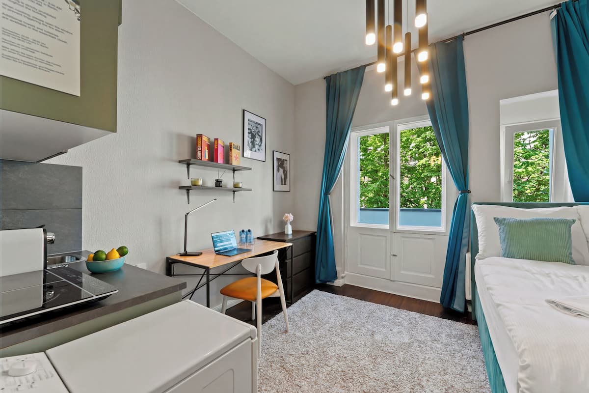 A modern bedroom with a bed, a desk, a laptop, and a window with curtains.