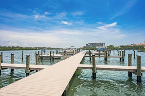 Eine hölzerne Pier erstreckt sich in ruhiges Wasser, mit Anlegestellen auf beiden Seiten, einem klaren Himmel und Gebäuden im Hintergrund.
