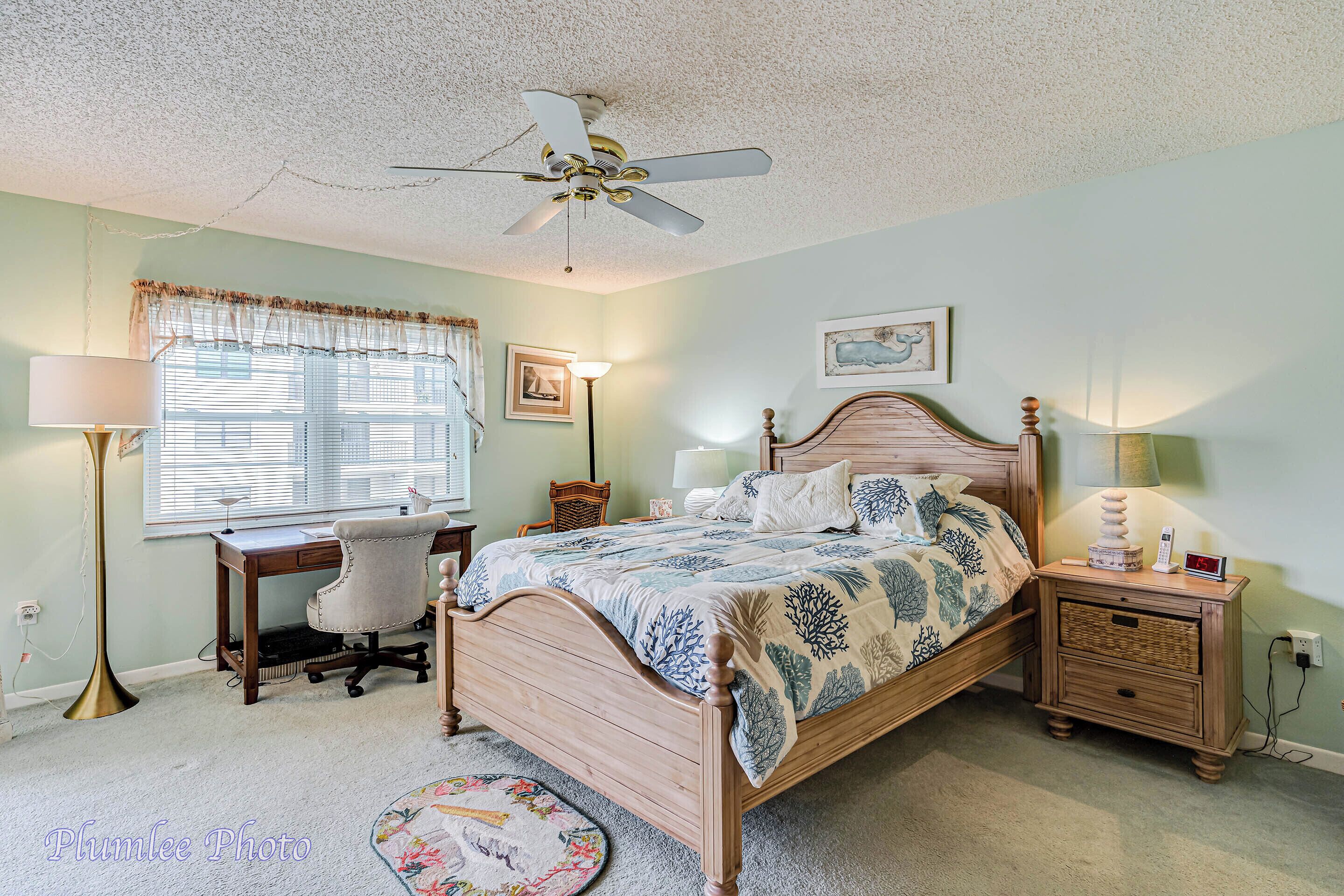 A bedroom with a wooden bed, a desk, a chair, a standing lamp, and a ceiling fan.