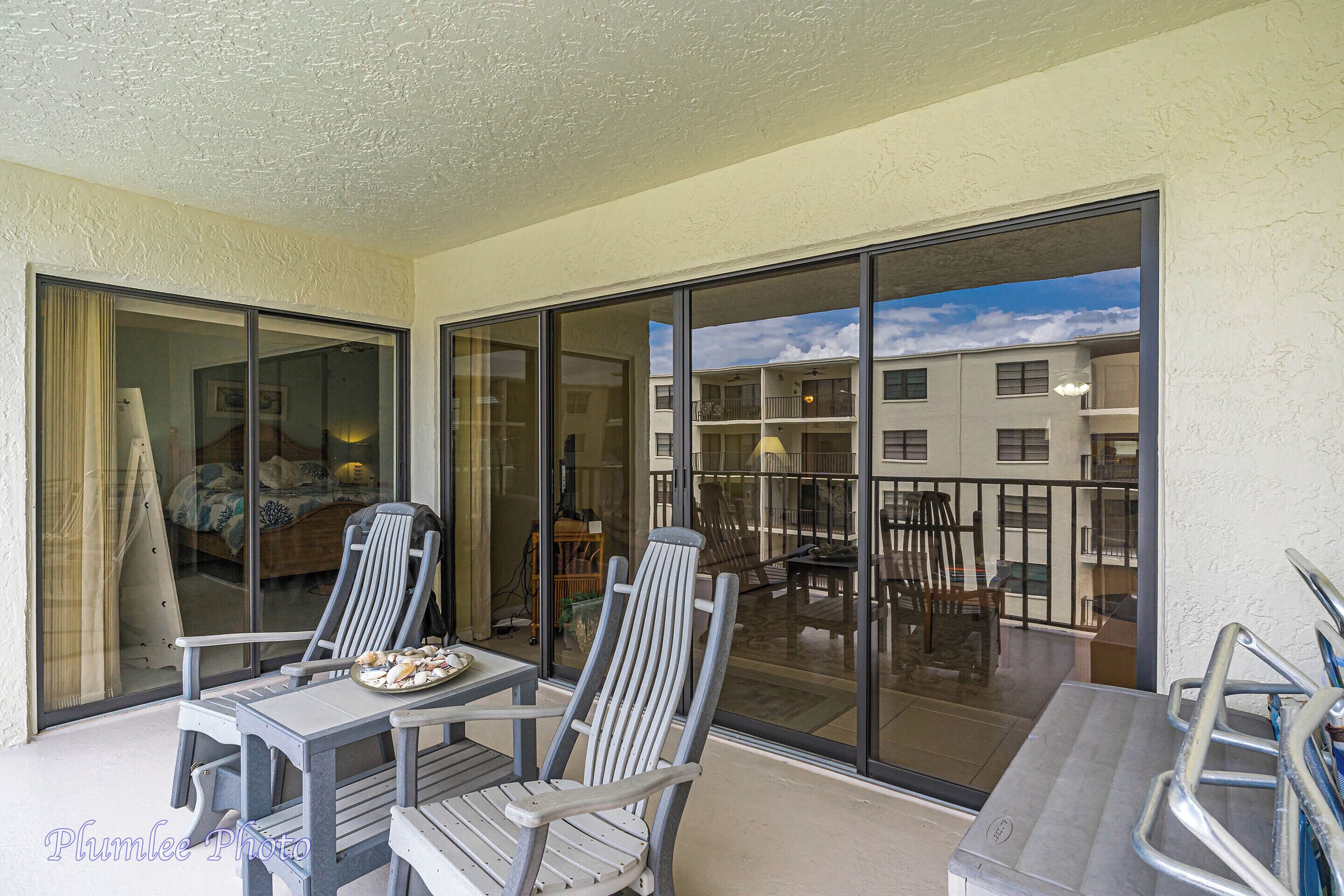 A balcony with two chairs and a table, large sliding glass doors, and a view of a building with multiple balconies.