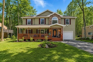 A two-story house with a front porch, a garage, and a landscaped yard. - Elegant Pocono Home with Hot Tub (Pocono Lake)