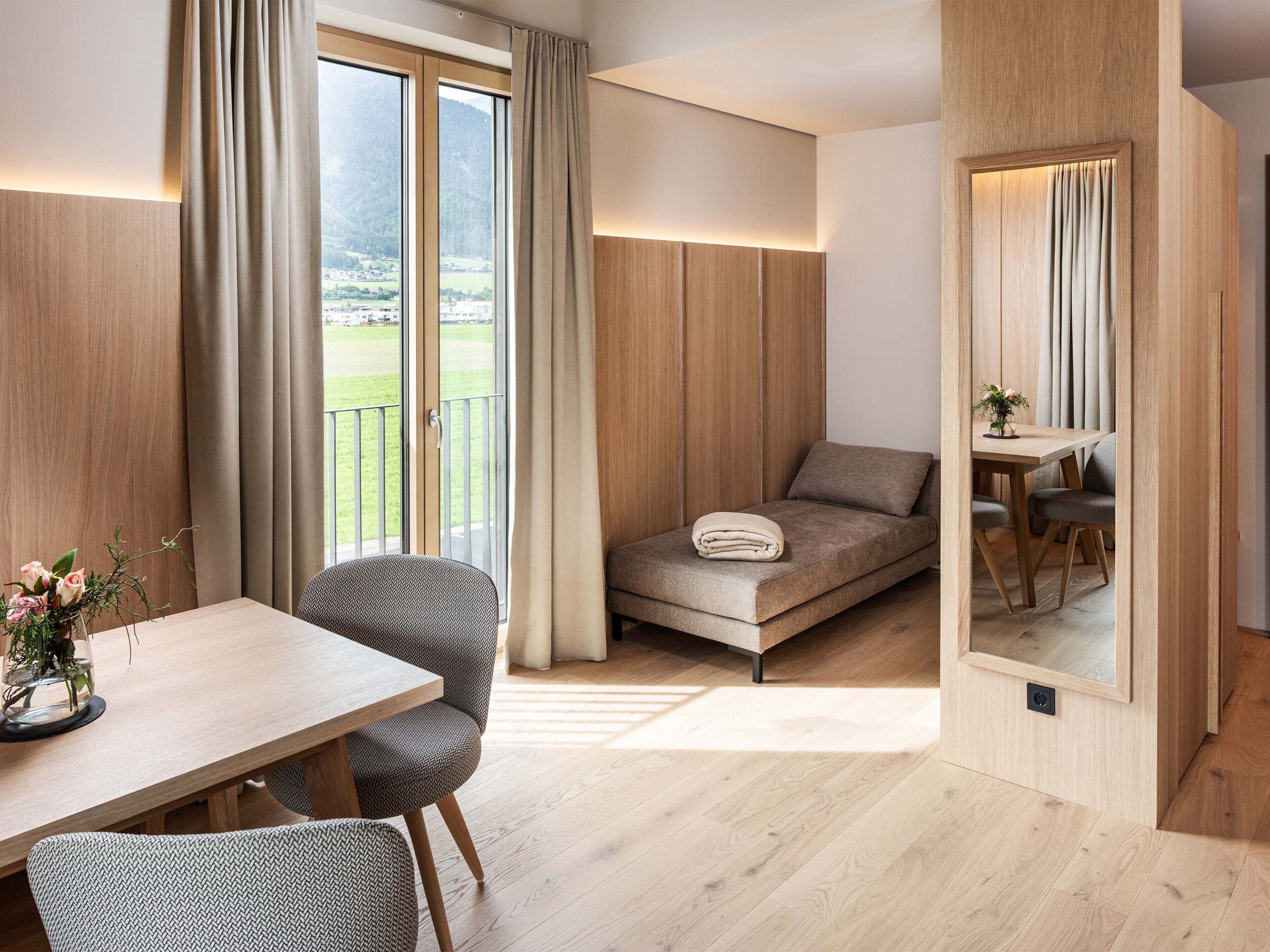 Una habitación moderna con sofá cama, una mesa de comedor con sillas y un balcón con vistas al campo.