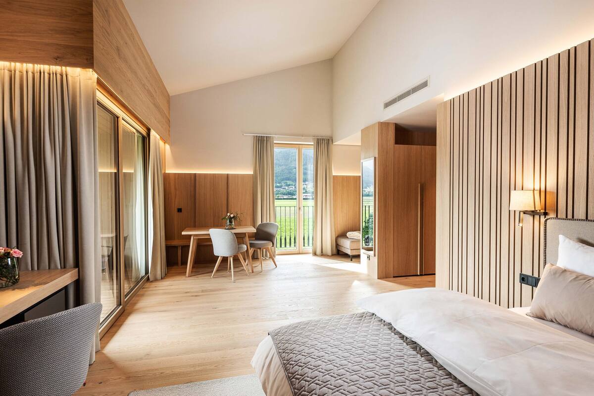 Une chambre d’hôtel moderne dotée d’un grand lit, d’un bureau avec deux chaises, d’un coin repas et offrant une vue sur l’extérieur.