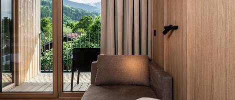 A modern room with a large sliding glass door leading to a balcony, a sofa with a folded blanket, and a wooden wall.