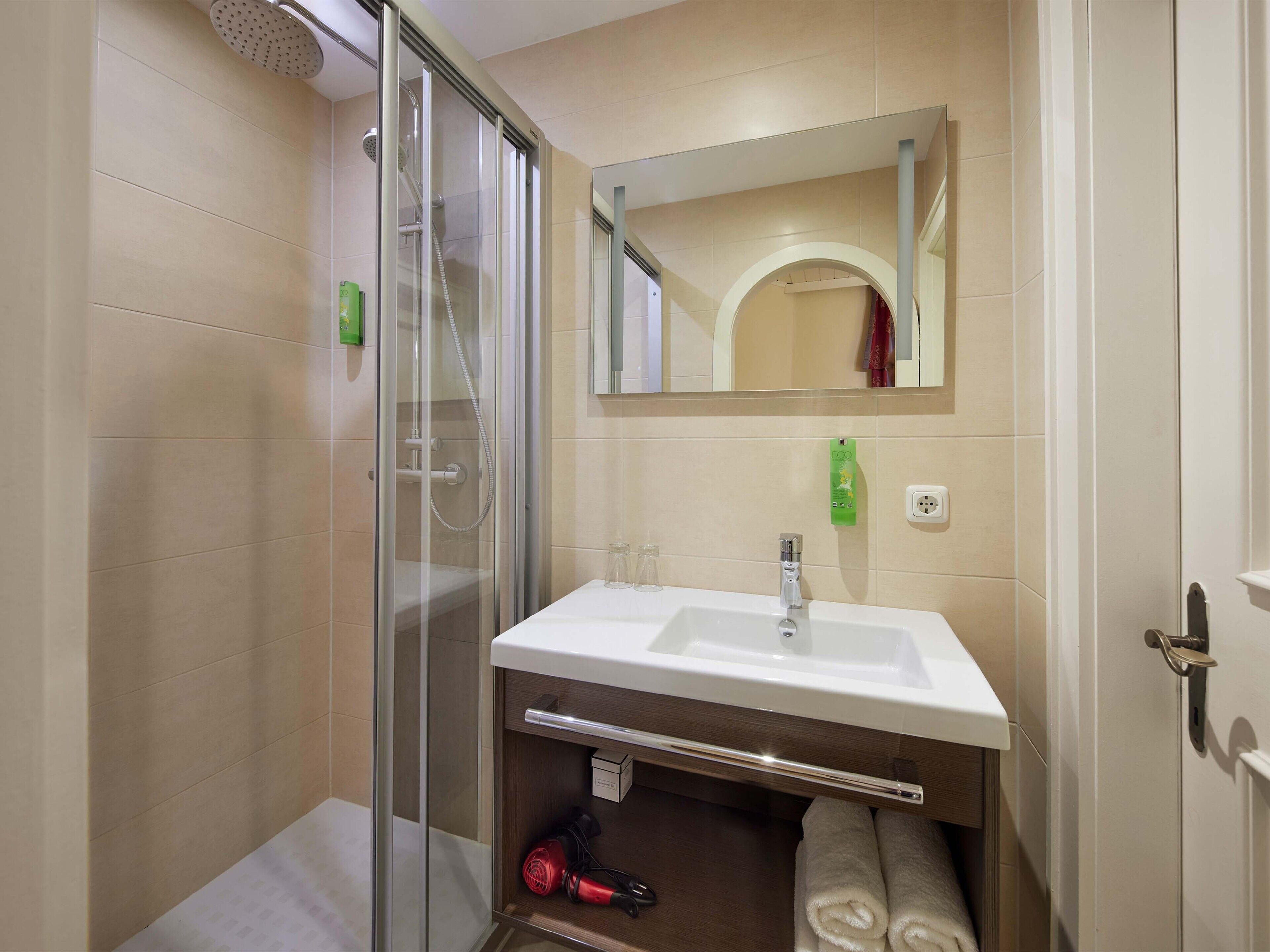 A modern bathroom with a glass-enclosed shower, a white sink, and a mirror above it.