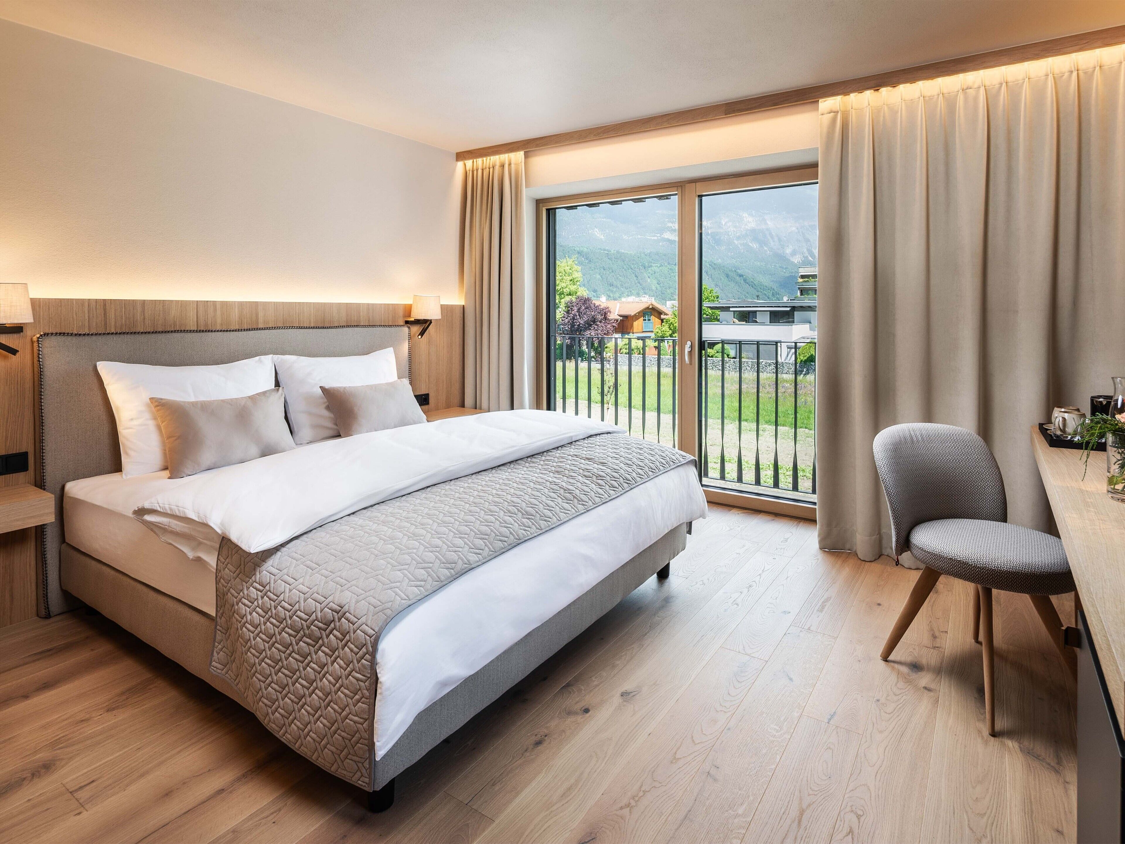 Une chambre d’hôtel moderne, dotée d’un grand lit, d’un bureau et offrant une vue sur un paysage montagneux par la fenêtre.